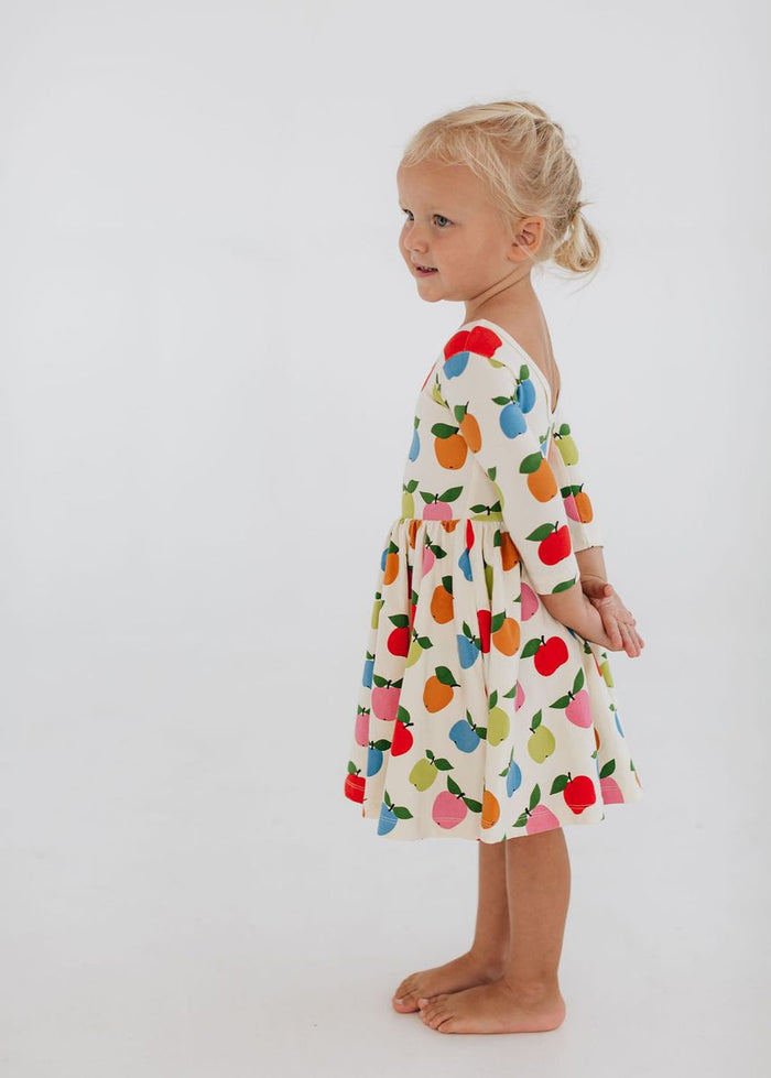 Child wearing a colorful fruit-patterned dress on a white background