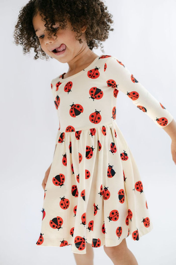 Child wearing a cream dress with red ladybug patterns on a white background