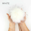 Hands holding a 6-inch faux fur pom pom in White with black-tipped fibers and a ribbon tie showing the full fluffy size