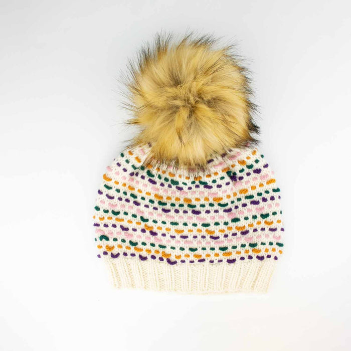 Colorwork knitted hat in cream with pink, green, purple, and ochre stitches topped with a Sable 6-inch faux fur pom pom on a white background