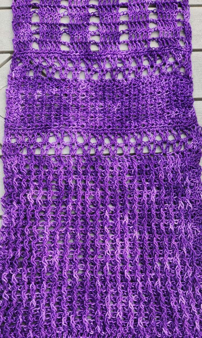Extreme close-up of the Galliano Revenge Wrap stitch detail showing the front and back post double crochet texture creating geometric checked boxes alongside open mesh sections in rich variegated purple yarn