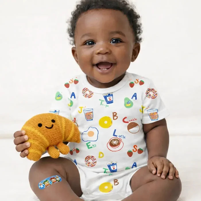 Baby wearing a colorful onesie holding a plush toy on a white background