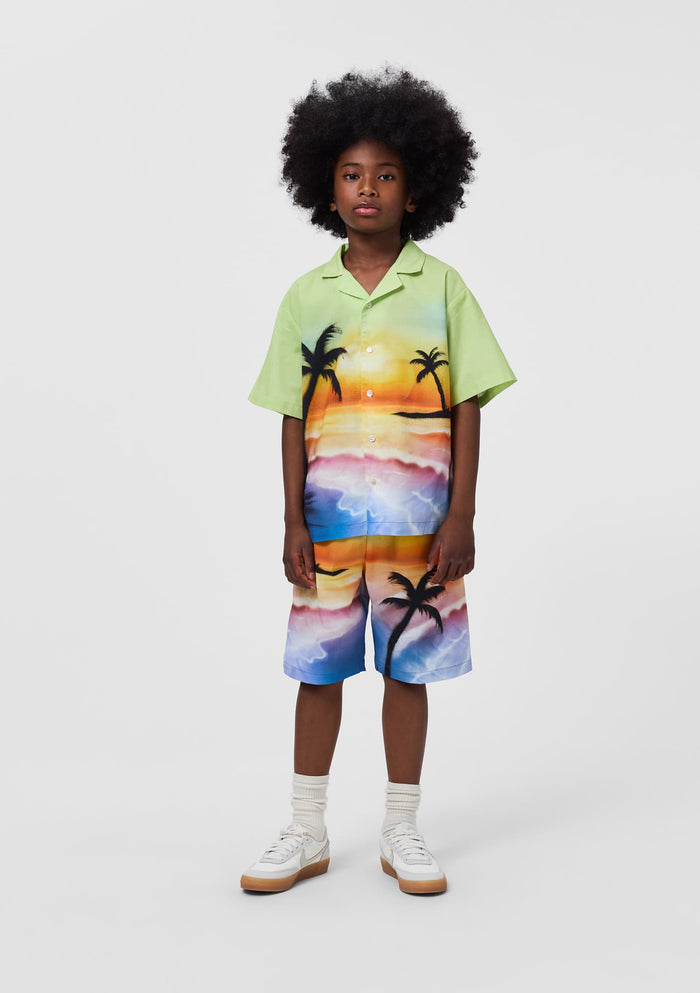 Child wearing a colorful shirt and shorts set with palm tree design on a white background