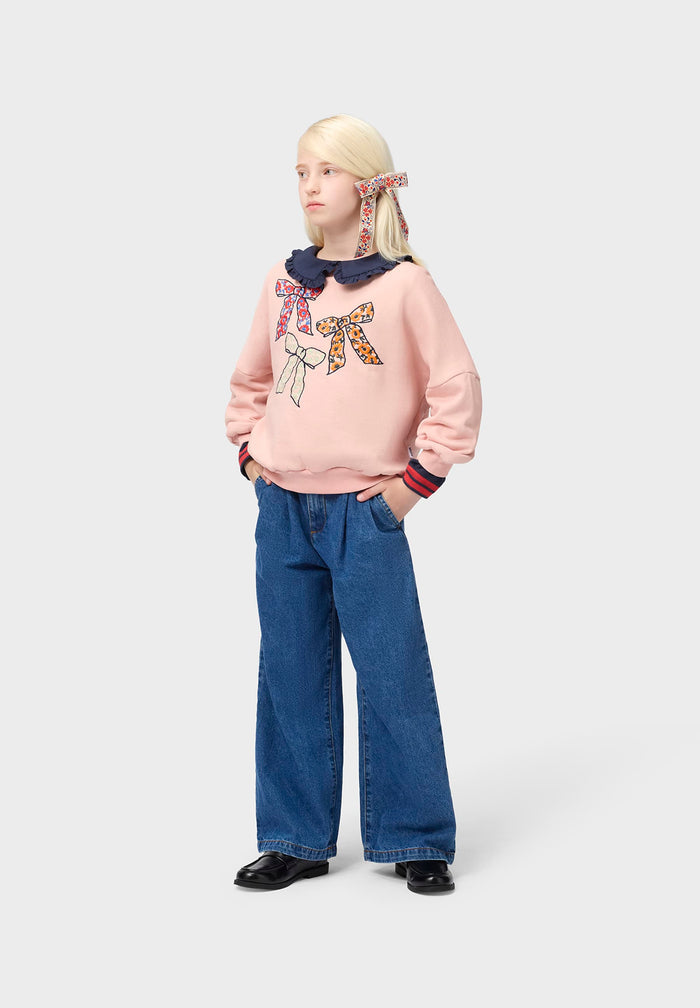Person wearing a pink sweater with bow design and blue jeans on a white background