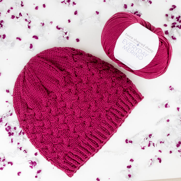 Sugar Beet pink cable-knit beanie with Everyday Merino yarn skein on confetti background