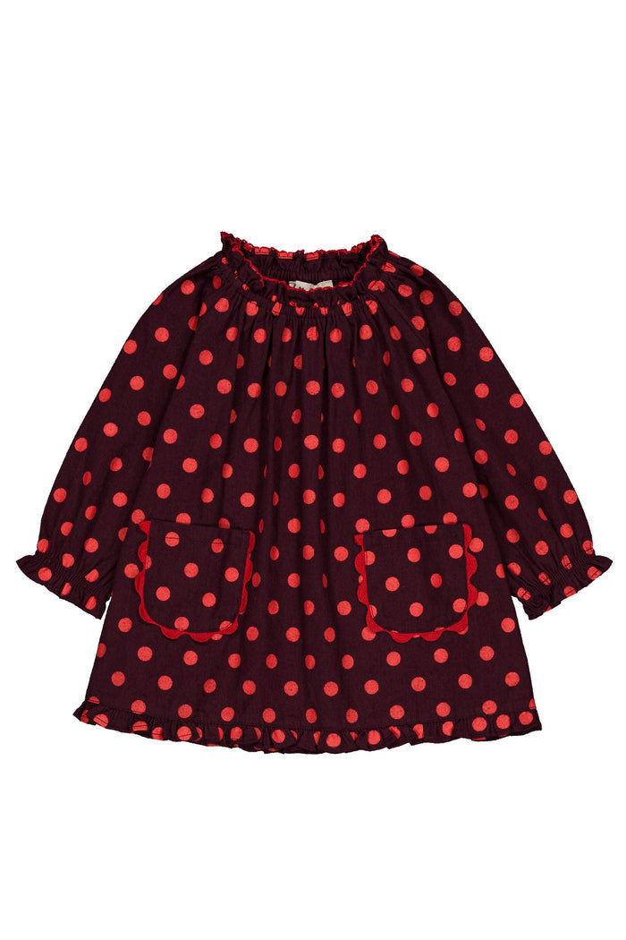 A long-sleeve children's dress with a red and polka dot pattern, featuring a gathered smocked neckline, ruffled cuffs, and two front patch pockets, shown flat on a white background.