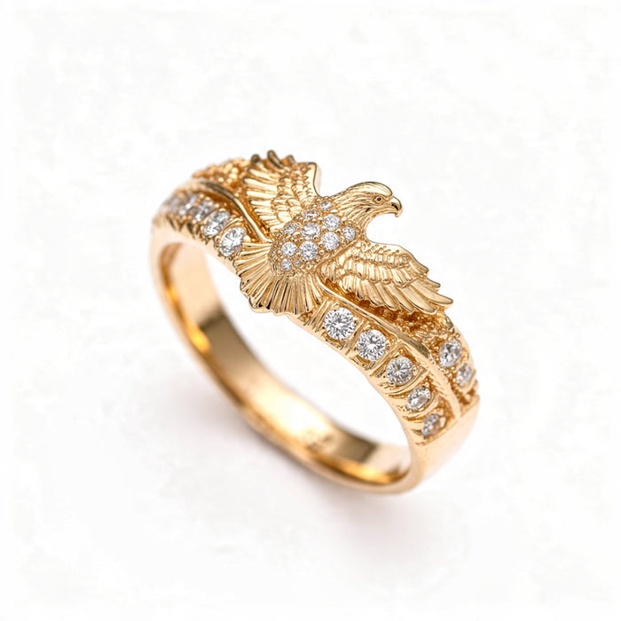A polished gold ring with a detailed eagle in flight and pavé crystal accents along the band, centered on a pure white background.