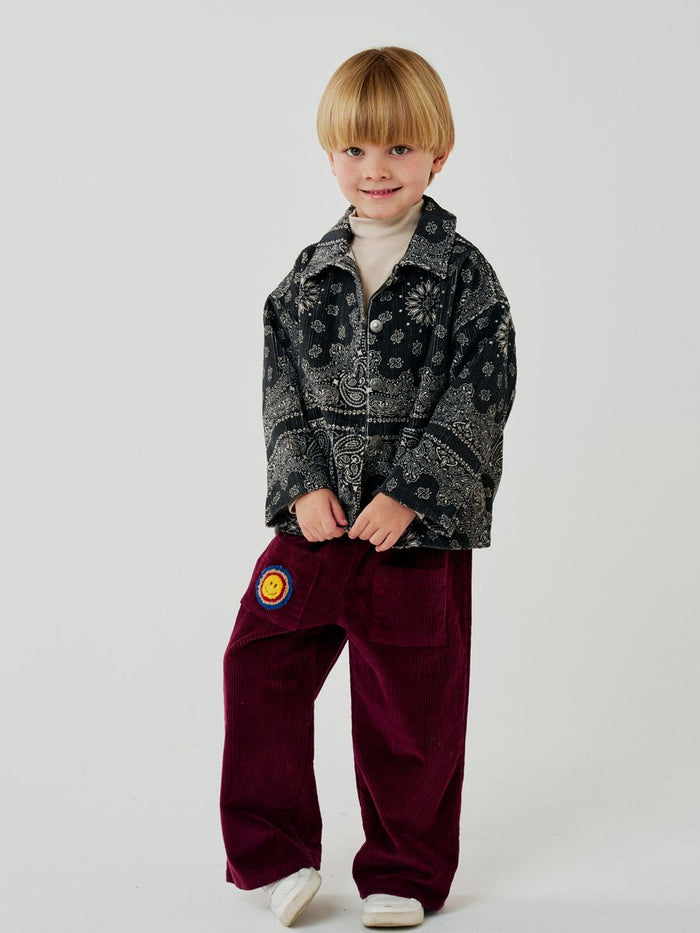 Child wearing a patterned shirt and burgundy pants with a logo on a white background