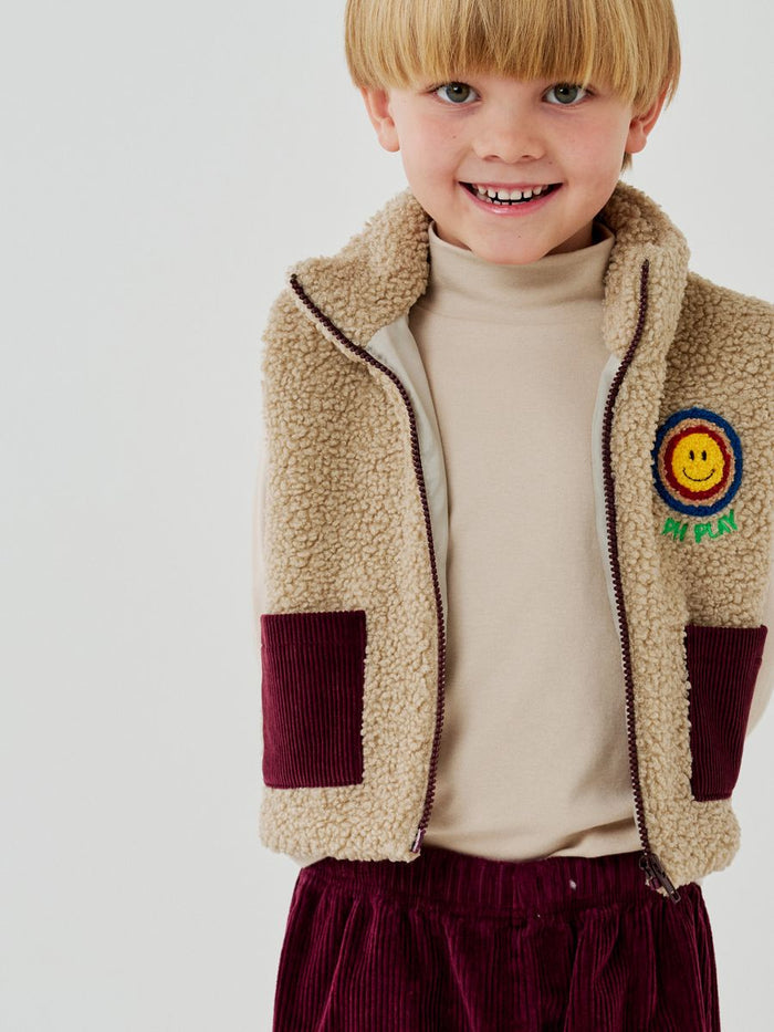 Child wearing a beige fleece jacket with a smiley face patch on a white background