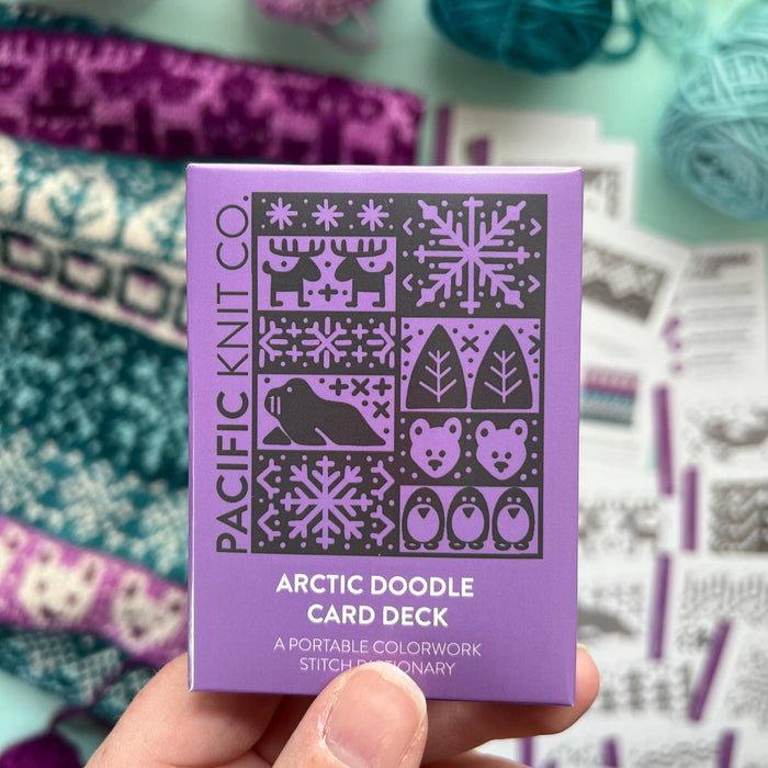 Hand holding the purple Arctic Doodle Card Deck by Pacific Knit Co tuckbox