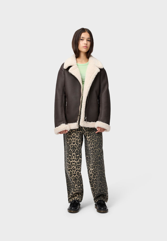 Person wearing a black leather jacket with white fur lining and leopard print pants on a white background