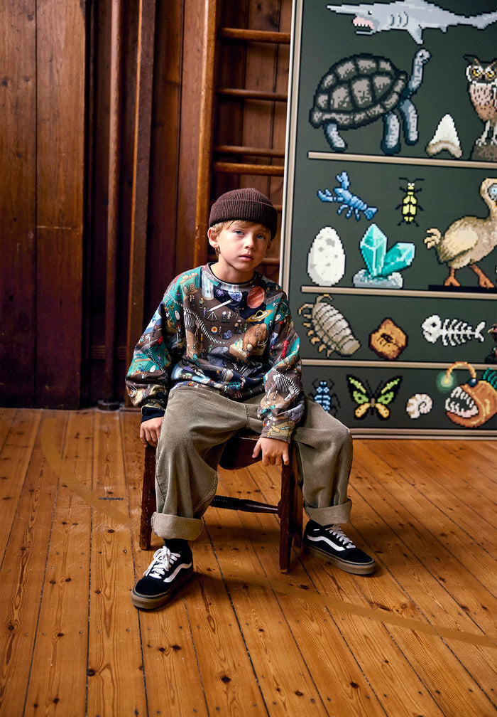 Child sitting on a chair in front of a chalkboard with educational drawings.