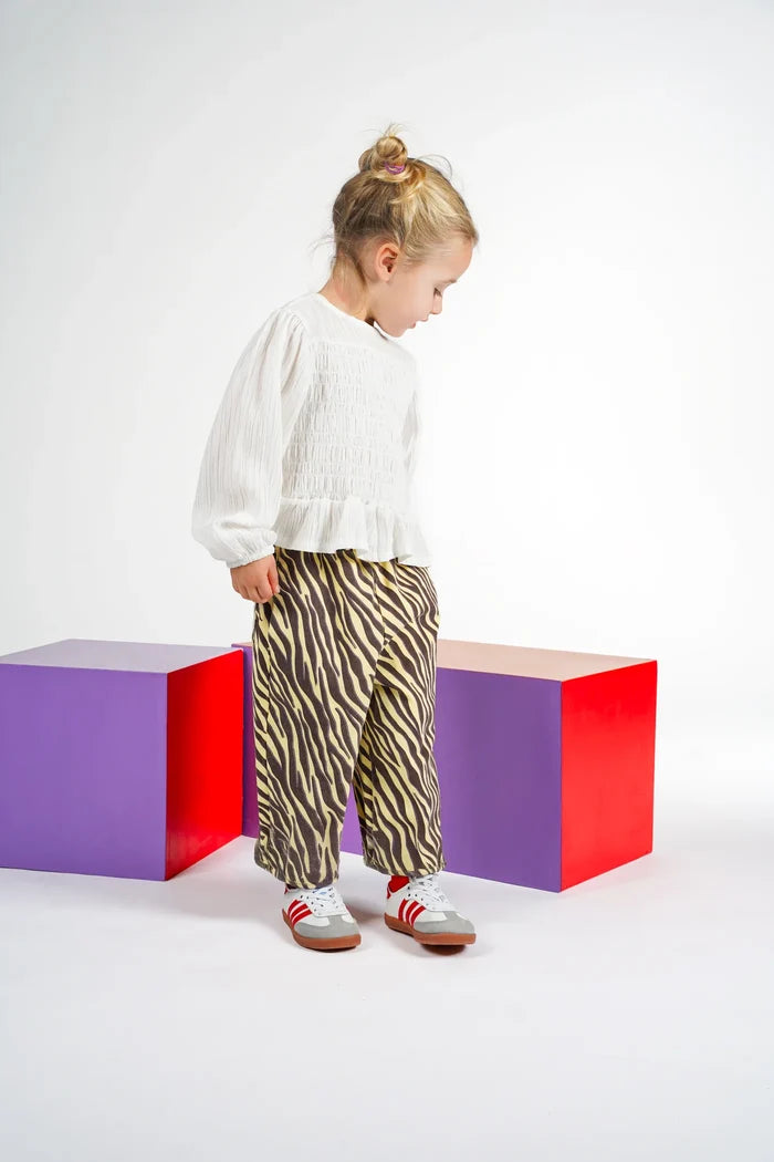 child wearing yellow and brown zebra stripe pants with white blouse in front of purple and red cubes on white background