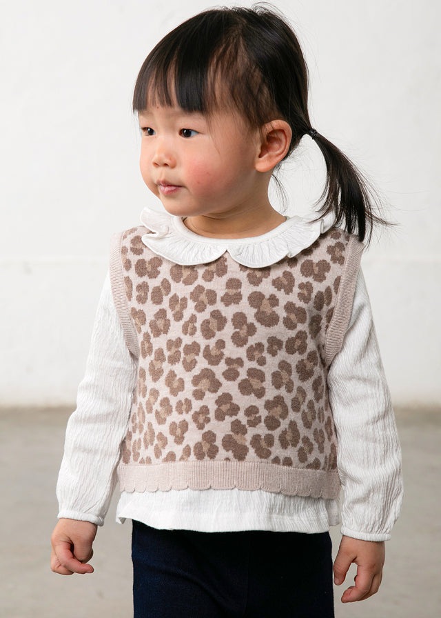 Child wearing a patterned vest over a white shirt with a plain background