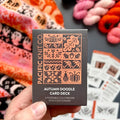 Hand holding the orange and black Autumn Doodle Card Deck by Pacific Knit Co tuckbox