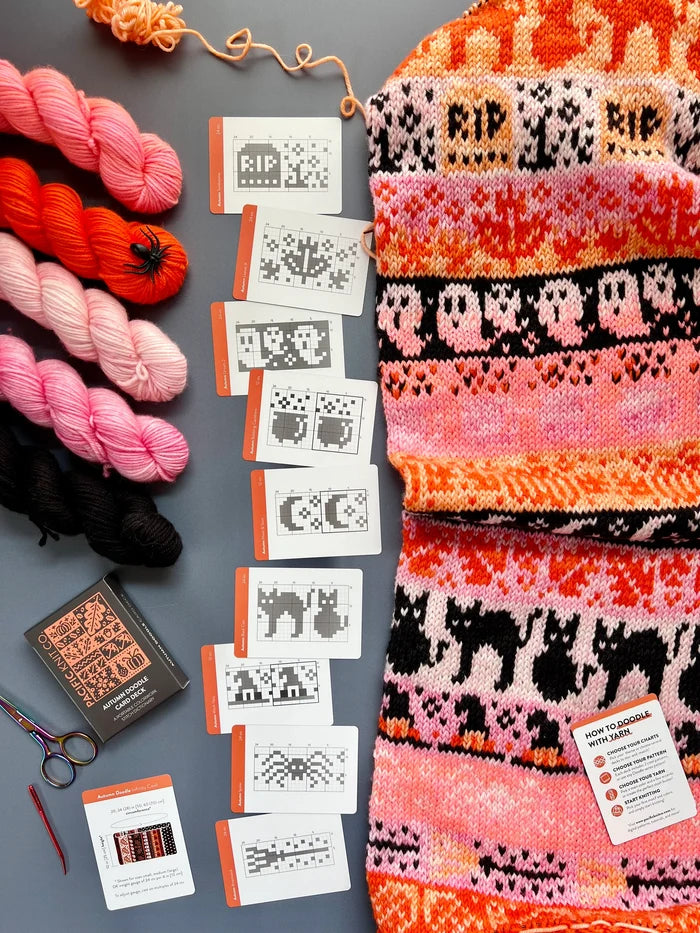 Autumn Doodle chart cards laid out beside a pink and orange Halloween colorwork knit and mini skeins
