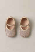 Pair of glittery baby shoes on a beige background