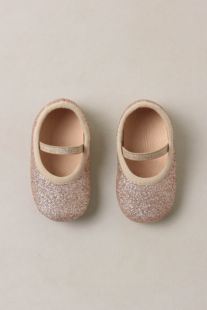 Pair of glittery baby shoes on a beige background