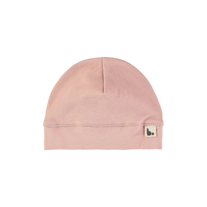 A light pink knit beanie hat with a small square brand patch on the folded cuff, shown against a plain white background.