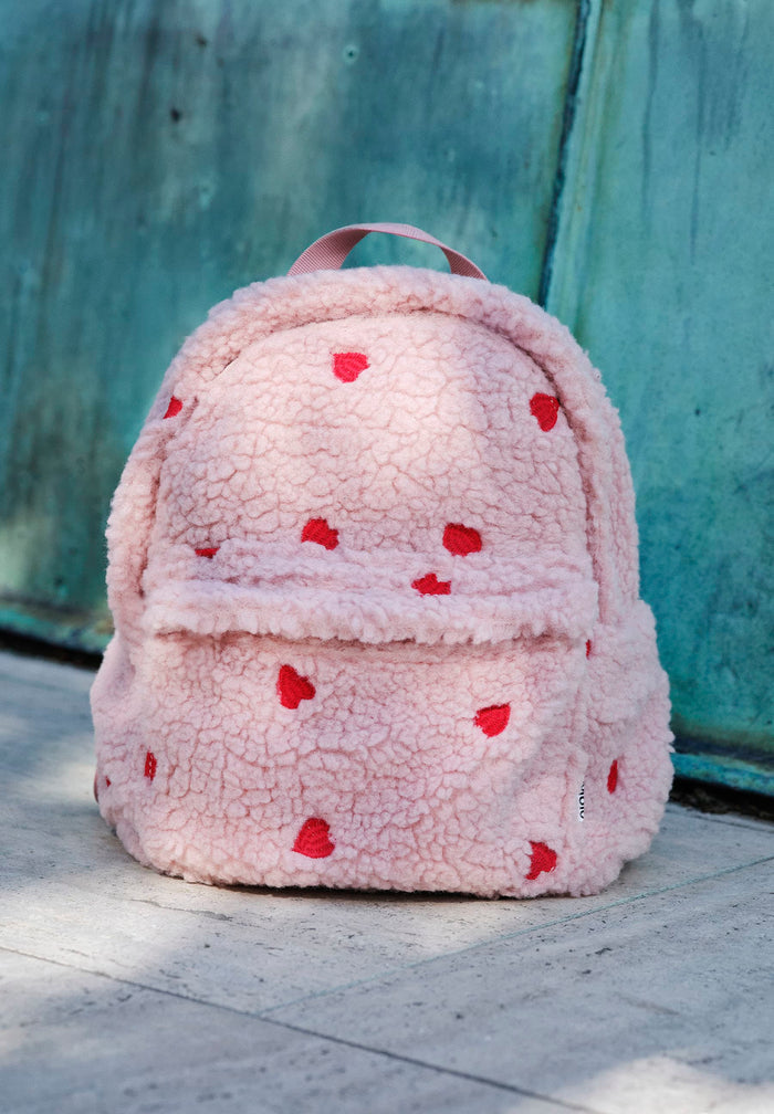 Pink fluffy backpack with red heart patterns on a concrete surface.