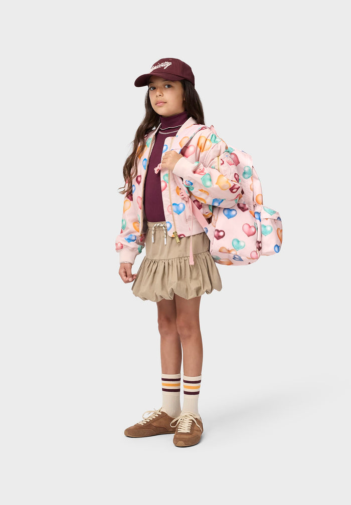 Child wearing a colorful heart-patterned jacket with a backpack on a white background