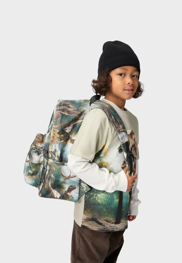 Child wearing a backpack with a dino design on a plain background
