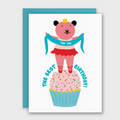 A white greeting card with a turquoise envelope behind it, featuring a cartoon pink bear dressed as a ballerina standing on a cupcake and holding a turquoise banner that reads 'FOR YOU'. The card also says 'THE BEST BIRTHDAY!' in turquoise text.