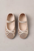 Pair of glittery ballet flats with bow details on a beige background