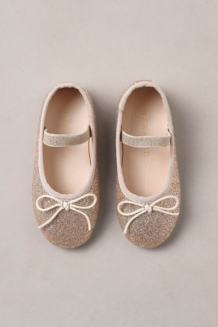 Pair of glittery ballet flats with bow details on a beige background