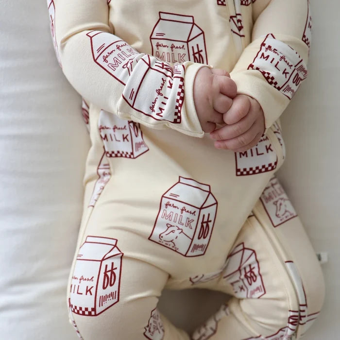 Baby in a cream-colored outfit with red milk carton patterns on a white background