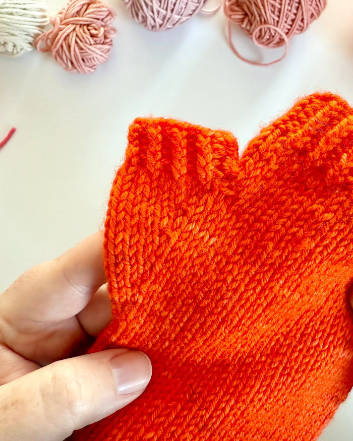 Hand wearing an orange Base Doodle Fingerless Mitt showing the thumb gusset