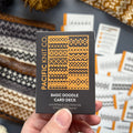 Hand holding the orange and black Basic Doodle Card Deck by Pacific Knit Co tuckbox