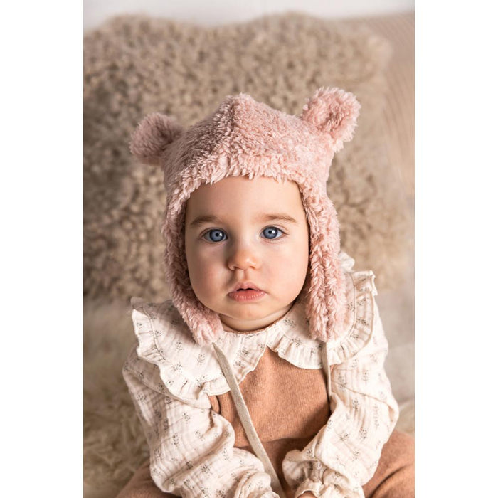 Baby wearing a pink bear hat with fluffy ears on a soft surface
