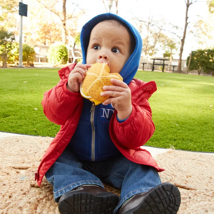 Child in a red jacket and blue hoodie eating a sandwich outdoors.