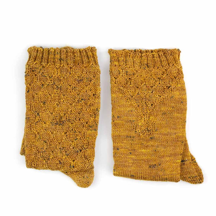 Flat lay of both Bees Knees knee-high socks folded side by side showing the front honeycomb lace pattern and the back stockinette in golden honey tweed yarn