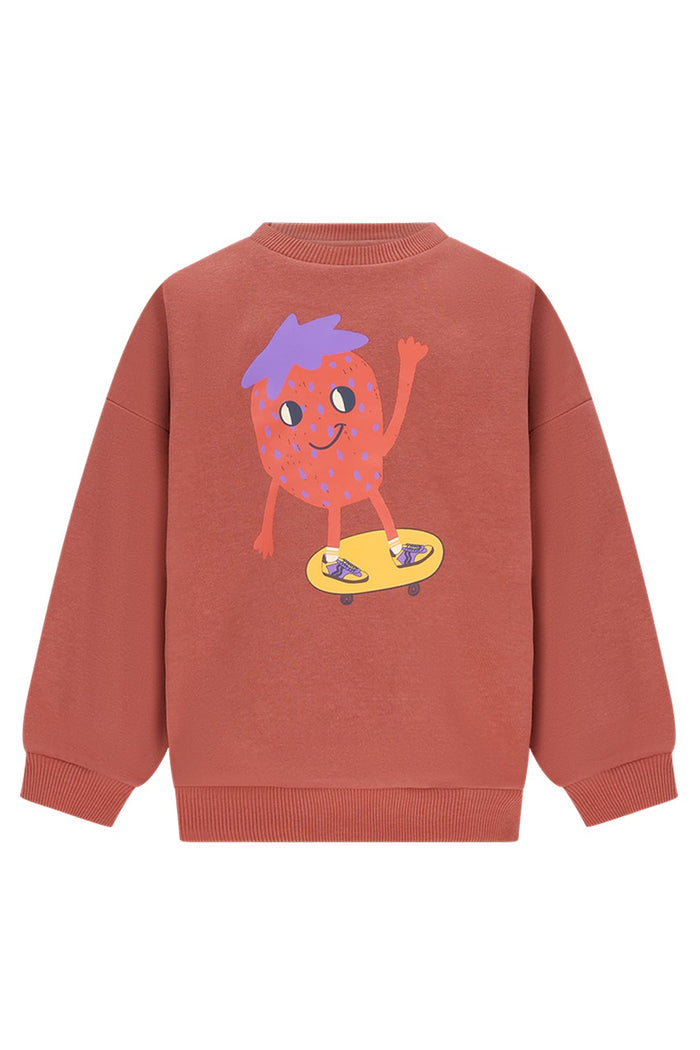 A terracotta-colored crewneck sweatshirt featuring a cartoon graphic of a smiling strawberry character with purple hair riding a yellow skateboard, shown against a plain white background.