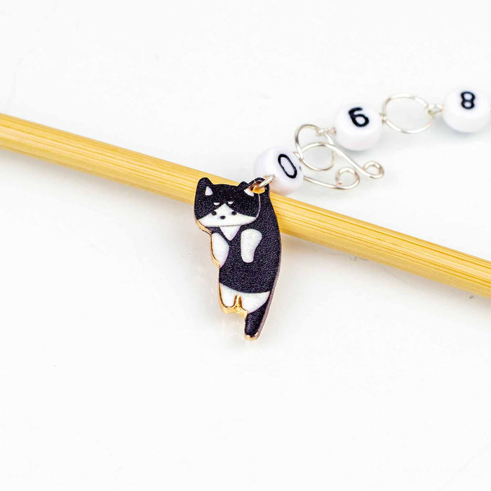 Black and white tuxedo cat enamel charm chain row counter on a bamboo knitting needle with numbered white counting chain beads on a white background