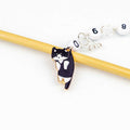 Black and white tuxedo cat enamel charm chain row counter on a bamboo knitting needle with numbered white counting chain beads on a white background