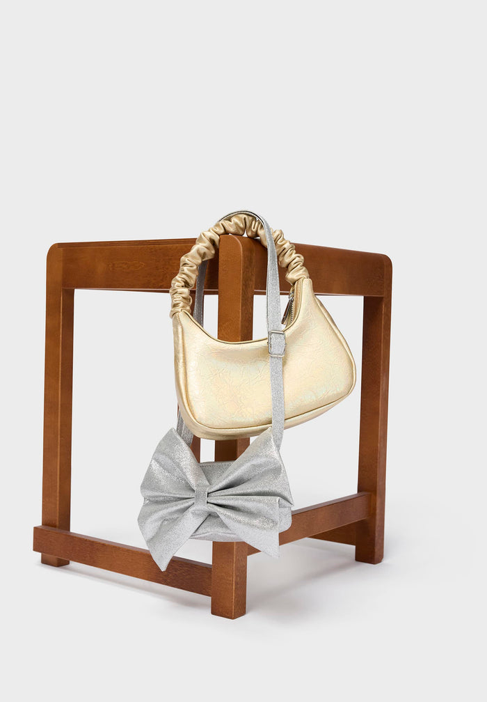 Cream-colored handbag and gray bow on a wooden stand against a white background