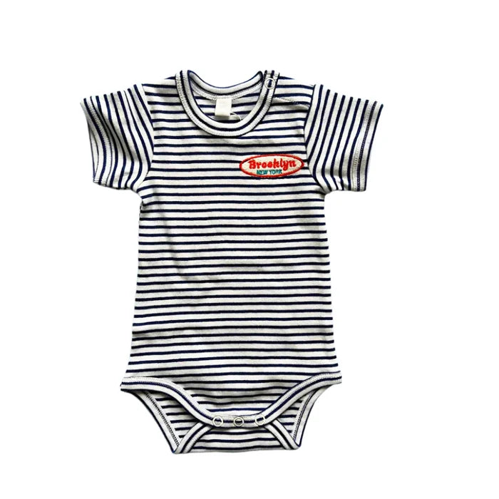 A striped organic cotton baby onesie with a 'Brooklyn, N.Y.' embroidered patch on the front.