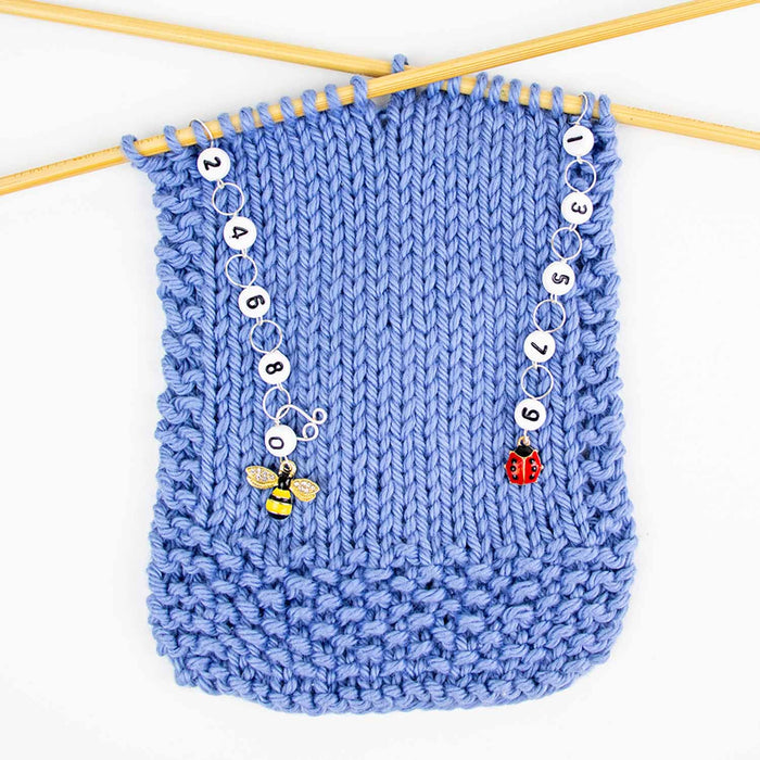 Bug friends odd even row counter set in use on blue knitting swatch with bee counter on left and ladybug counter on right