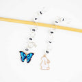 Two straight chain row counters on bamboo needle with blue enamel butterfly charm for even numbers and white enamel bunny charm for odd numbers