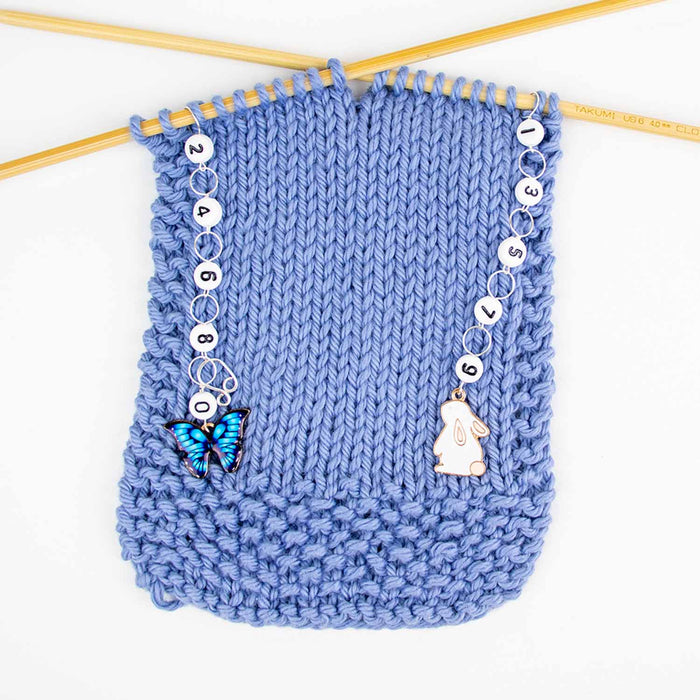 Bunnies and butterflies odd even row counter set in use on blue knitting swatch showing both chains hanging from needles