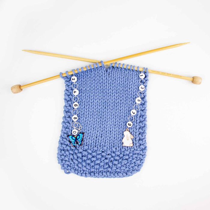 Wider view of bunnies and butterflies row counter set on blue knitting with bamboo needles crossed showing both counters in use