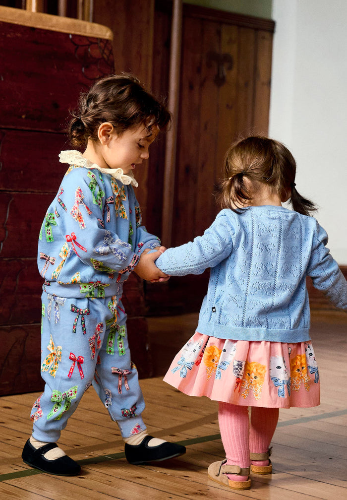 Two children in colorful outfits standing on a wooden floor.