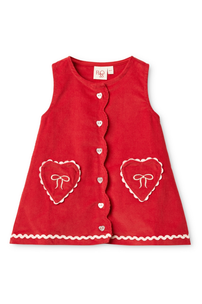 A red sleeveless children's dress with a scalloped front, decorative white heart outlines, bow details, and a button closure, shown flat on a white background.