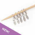 Five silver cast-on counting stitch markers numbered 20, 40, 60, 80, and 100 hanging from a bamboo knitting needle
