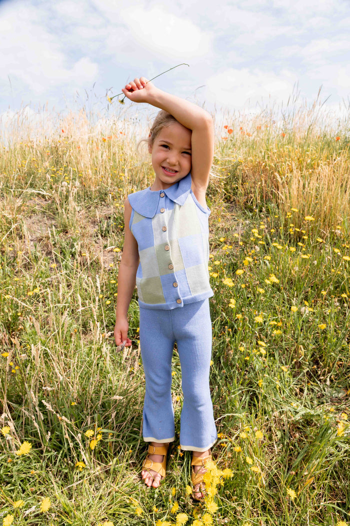 Child standing in a field of tall grass and wildflowers, holding a flower.