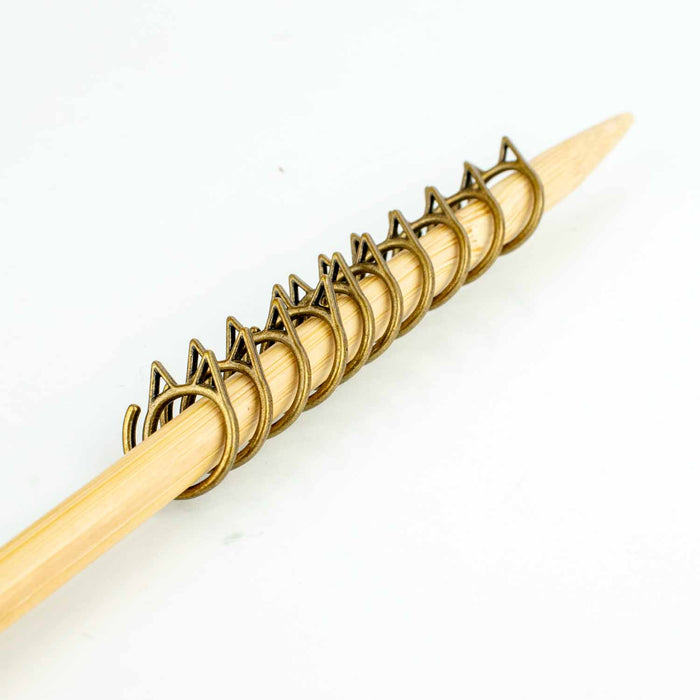 Row of bronze cat-face stitch markers lined up on bamboo knitting needle