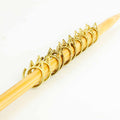 Row of gold cat-face stitch markers lined up on bamboo knitting needle